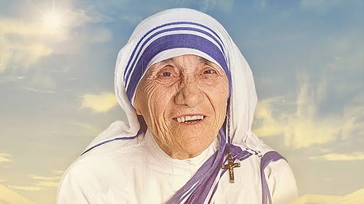 Madre Teresa de Calcutá, uma mulher idosa com um sorriso gentil, vestida com um sari branco com bordas azuis, segurando as mãos de uma criança