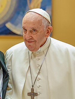 Papa Francisco, um homem idoso com cabelos brancos e óculos, vestindo vestes papais brancas, sorrindo e acenando para uma multidão em frente à Basílica de São Pedro no Vaticano.